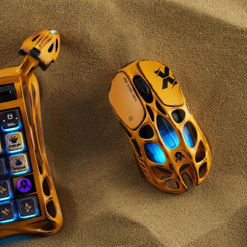 GravaStar Mercury X Pro 8K Battle Worn Yellow gaming mouse beside a matching keyboard on sand
