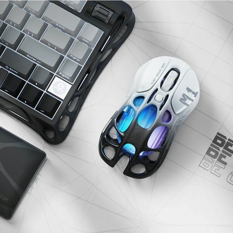 GravaStar Mercury M1 Pro gaming mouse on a desk beside a keyboard, showing blue and purple lighting through the skeletal frame